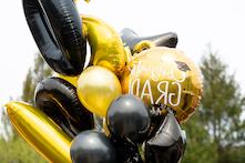 image of various sizes of black and gold balloons, one has the text congrats grad! on it